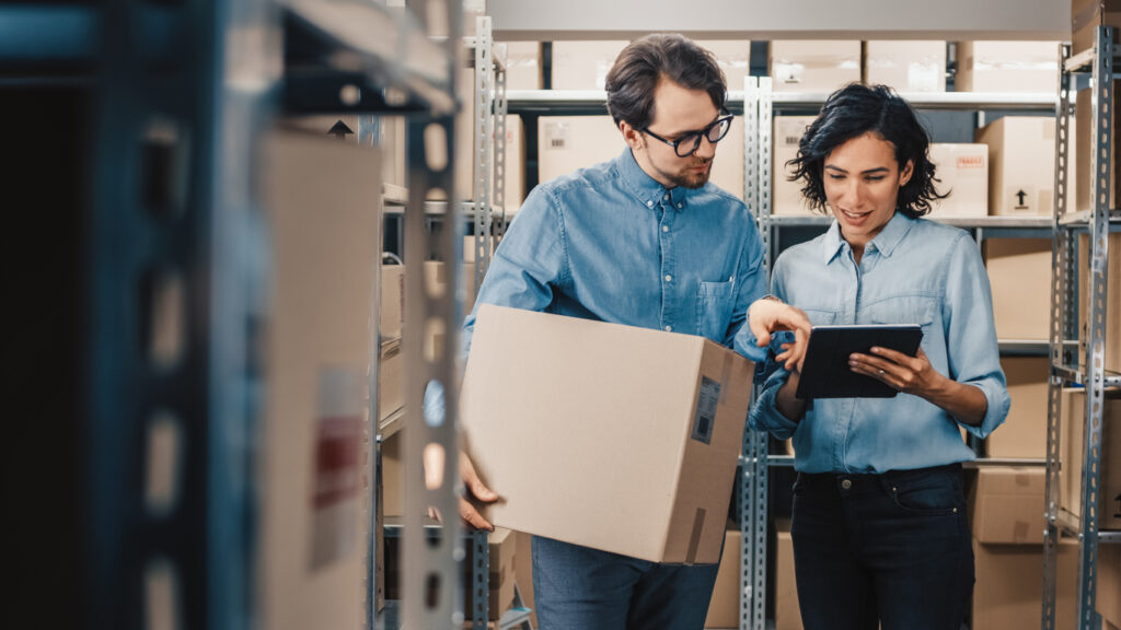 Female Inventory Manager Shows Digital Tablet Information to a Worker Holding Cardboard Box, They Talk and Do Work. In the Background Stock of Parcels with Products Ready for Shipment. small business audit checklist