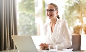 woman smiling as she's seated behind a laptop - jobs AI can't replace featured image