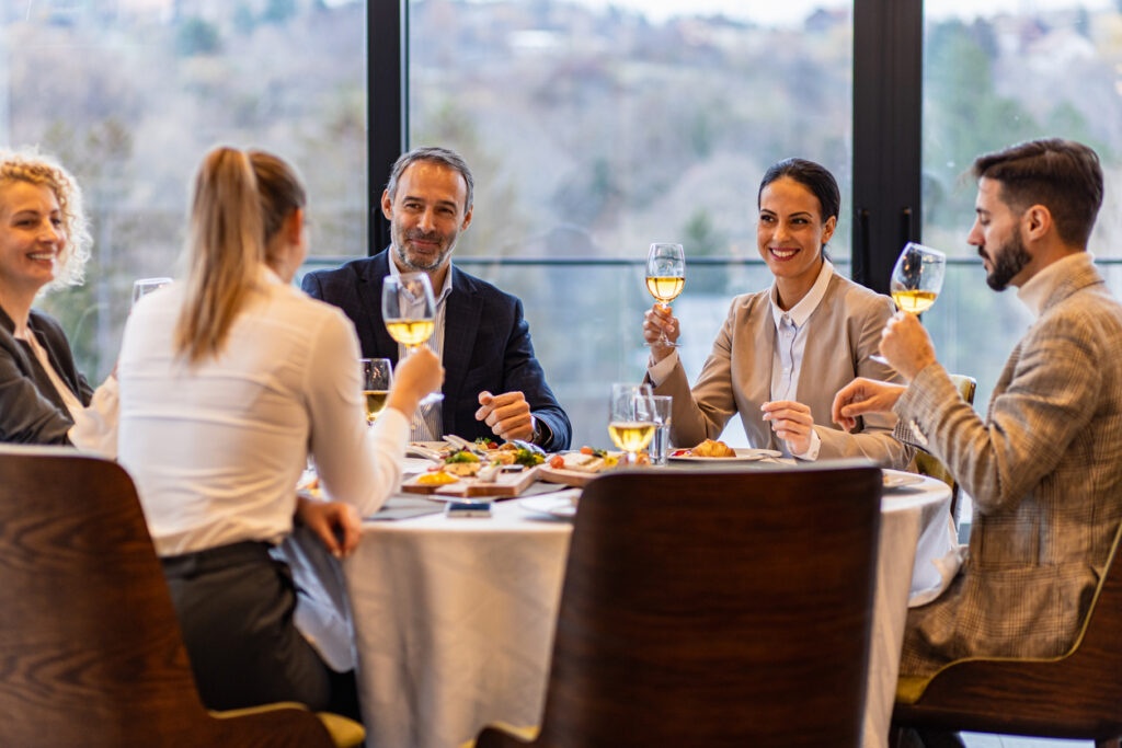 how to entertain clients Smiling coworkers in restaurant talking during business lunch.