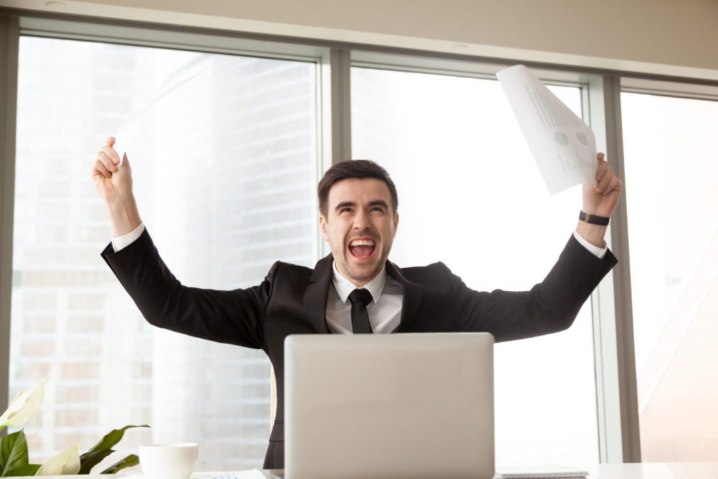  Excited businessman waving business papers in hands and screaming loudly with joy at desk in office. Happy boss celebrating with vivacity company success. CEO enjoying growth of Financial indicators boss new skills