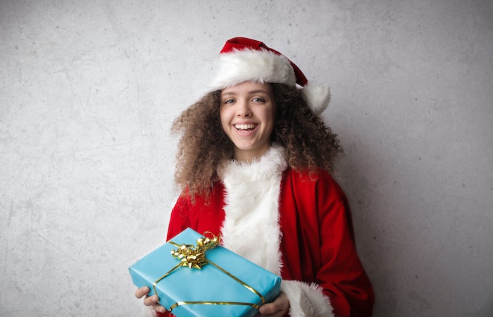 Young Child in Red Santa Hat Holding Blue Christmas Present - charities to donate to for Christmas