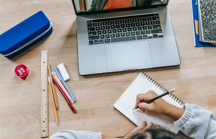 Clever schoolgirl doing homework in notebook while having online lesson - job courses online