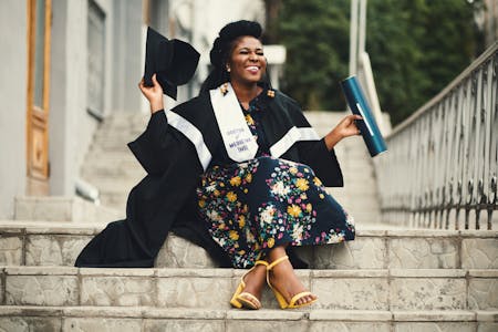 behavioral science degree online - graduating woman sits on steps with cap and gown