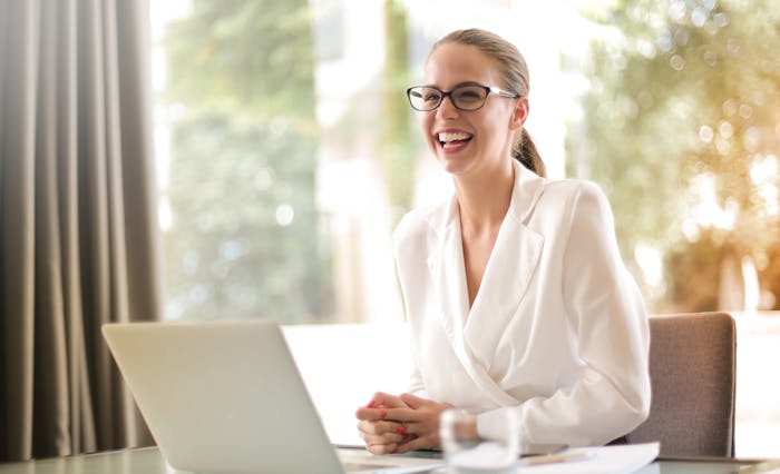 woman smiling as she's seated behind a laptop - jobs AI can't replace featured image