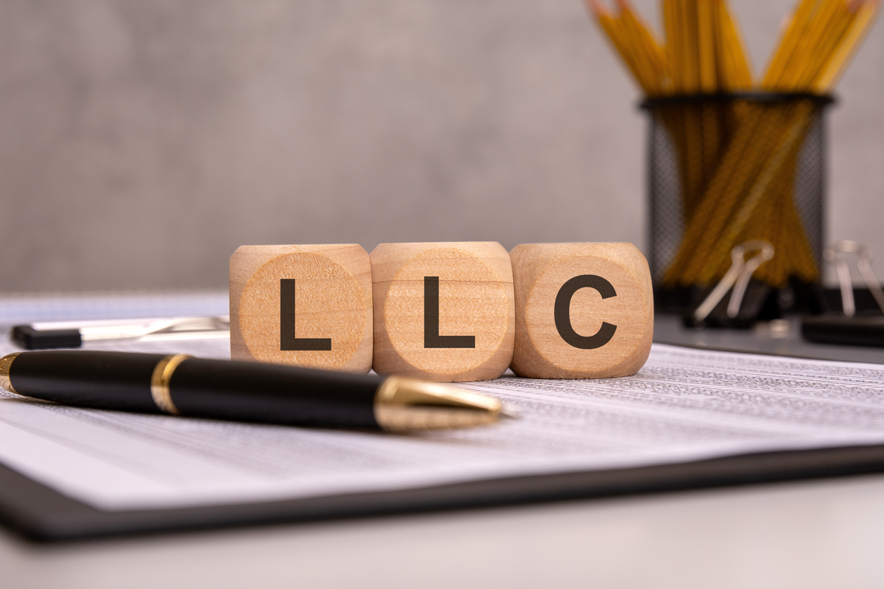 wooden cubes displaying the abbreviation LLC on a work desk with financial documents, a pen, and office supplies. the image represents limited liability company concepts, business structures, and legal entities How to Start an LLC in 2026